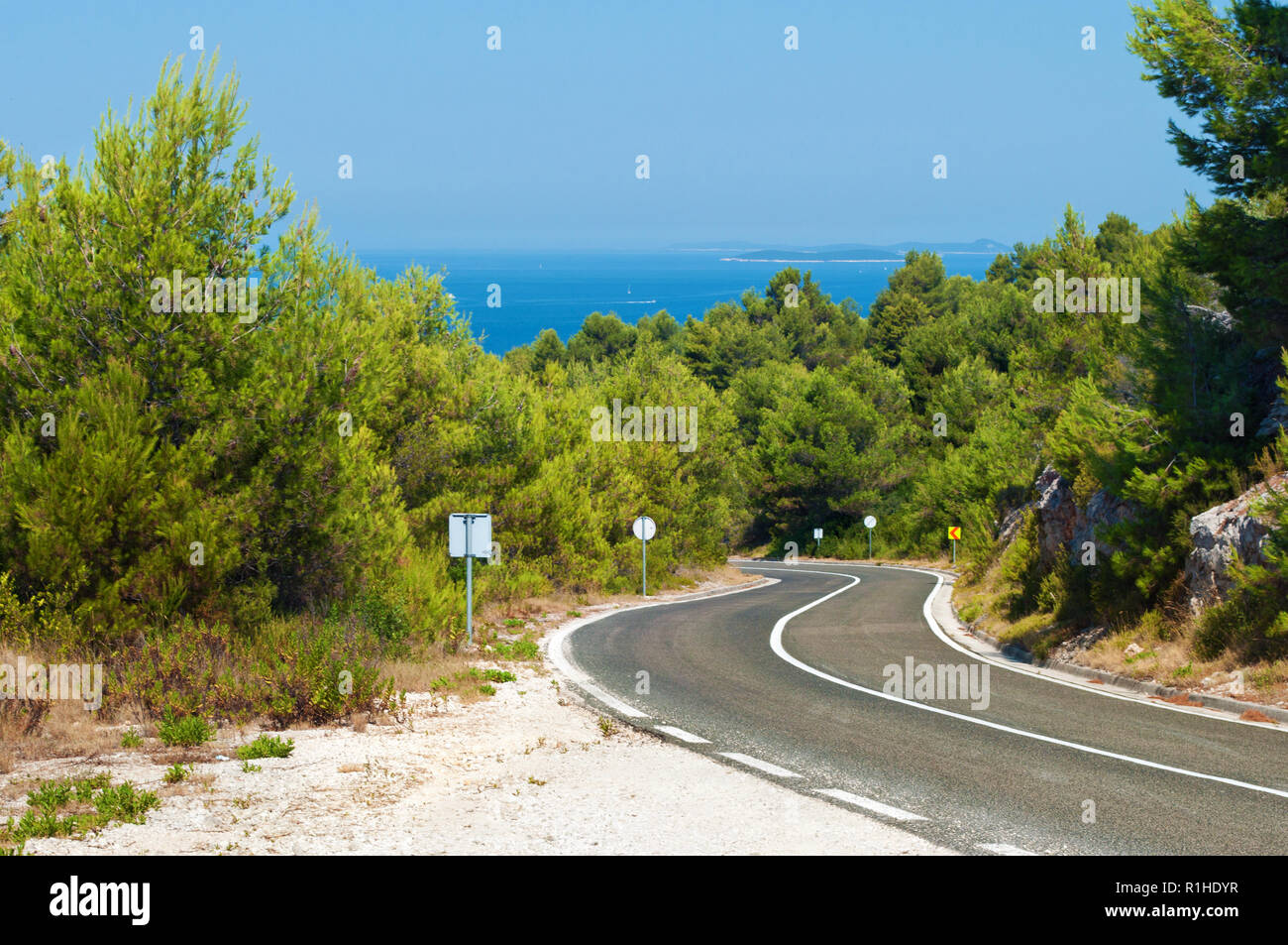 Leere Straße Wicklung unter den Felsen und grünen Hügeln mit Pinien gegen den azurblauen Meer an einem warmen Sommertag. Blauen wolkenlosen Himmel auf der Rückseite. D Stockfoto