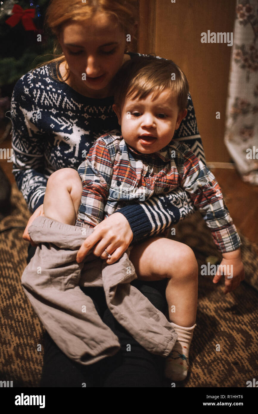 Mutter Dressing ihr Kind auf dem Boden zu Hause sitzen während Weihnachten Stockfoto