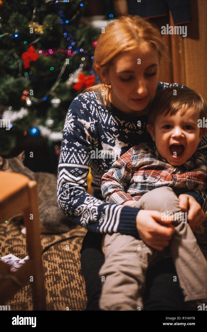 Mutter Dressing ihr Kind auf dem Boden zu Hause sitzen während Weihnachten Stockfoto