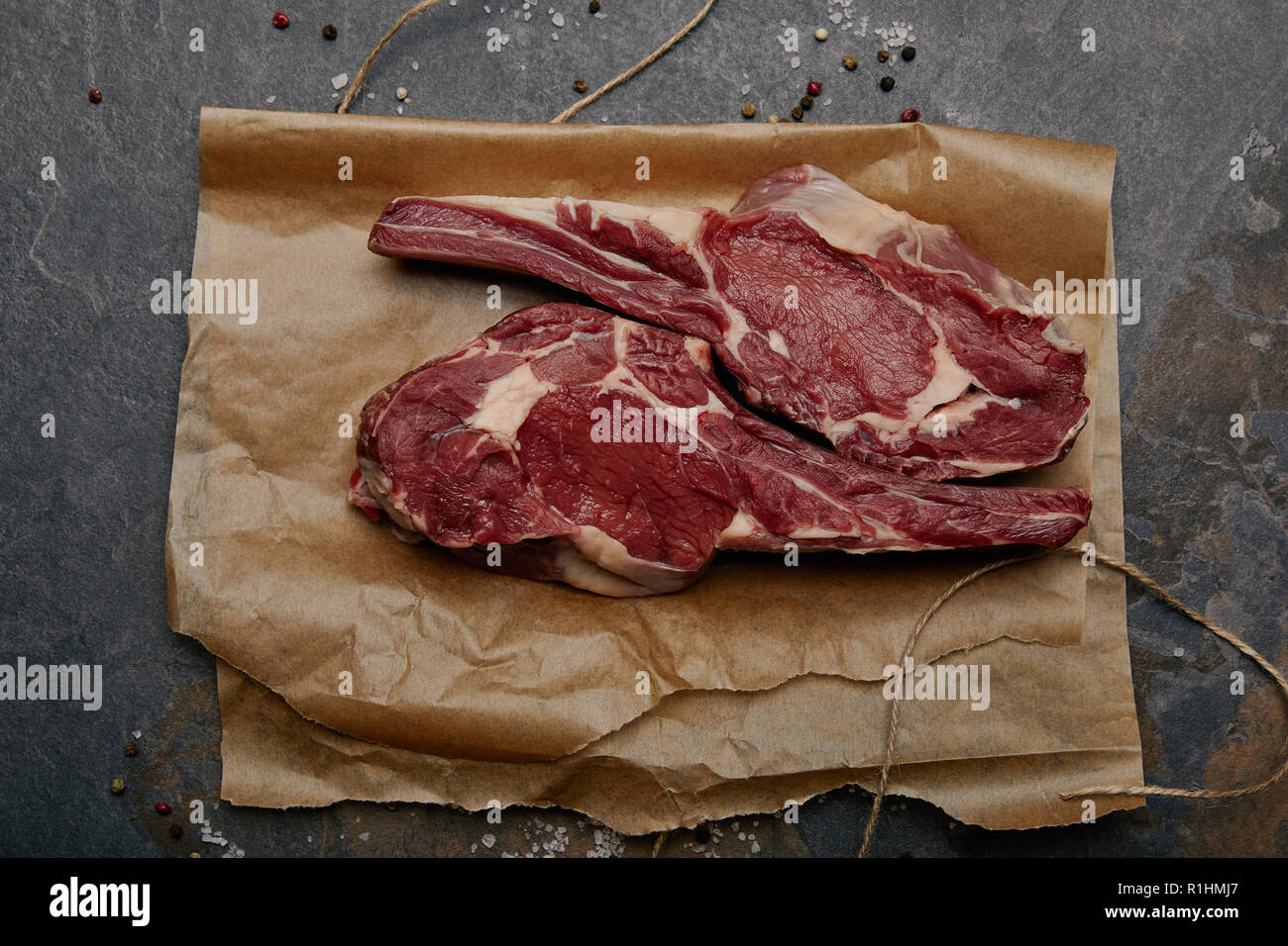 Blick von oben auf die Raw-Rib Eye Steaks auf Backpapier mit Gewürzen auf grauem Hintergrund Stockfoto