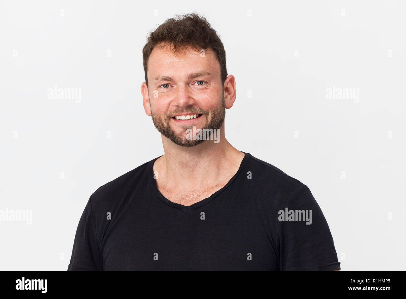 Stattlicher Mann mit schwarzen Shirt mit schönen Lächeln gegen den weißen Hintergrund posiert Stockfoto