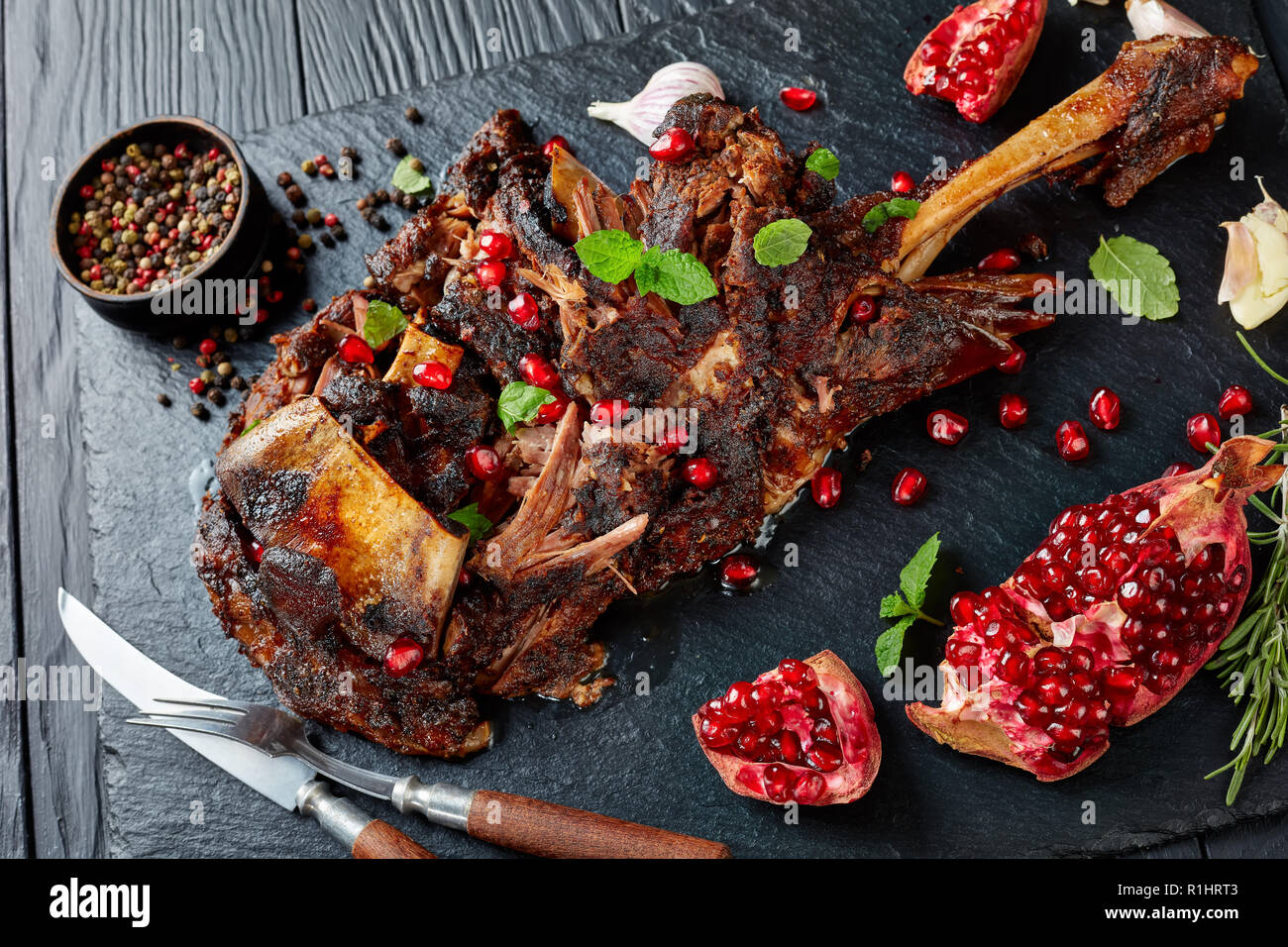 Ansicht von oben der köstlichen Braten zarte Lammkeule serviert mit Granatapfel Samen, Minze, Gewürze und Rosmarin auf schwarzem Schiefer Platte auf einer hölzernen Stockfoto