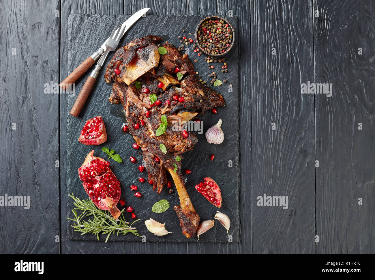 Ansicht von oben der köstlichen Braten zarte Lammkeule serviert mit Granatapfel Samen, Minze, Gewürze und Rosmarin auf schwarzem Schiefer Platte auf einer hölzernen Stockfoto