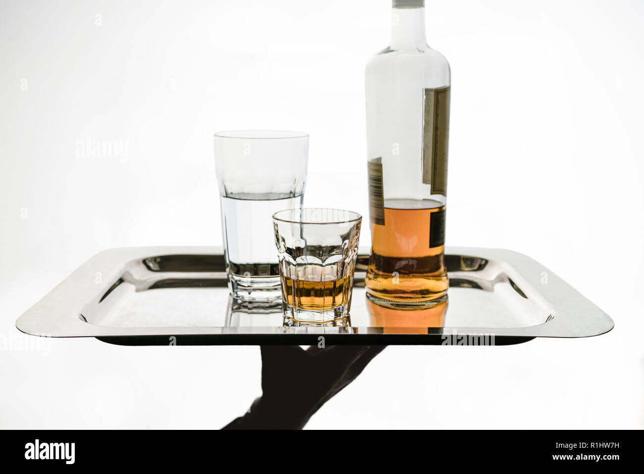 Die Kellnerhand bringt auf eine Silberplatte, ein Glas Wasser, ein Glas Alkohol und eine Flasche. Isolierter Kopierbereich. Stockfoto