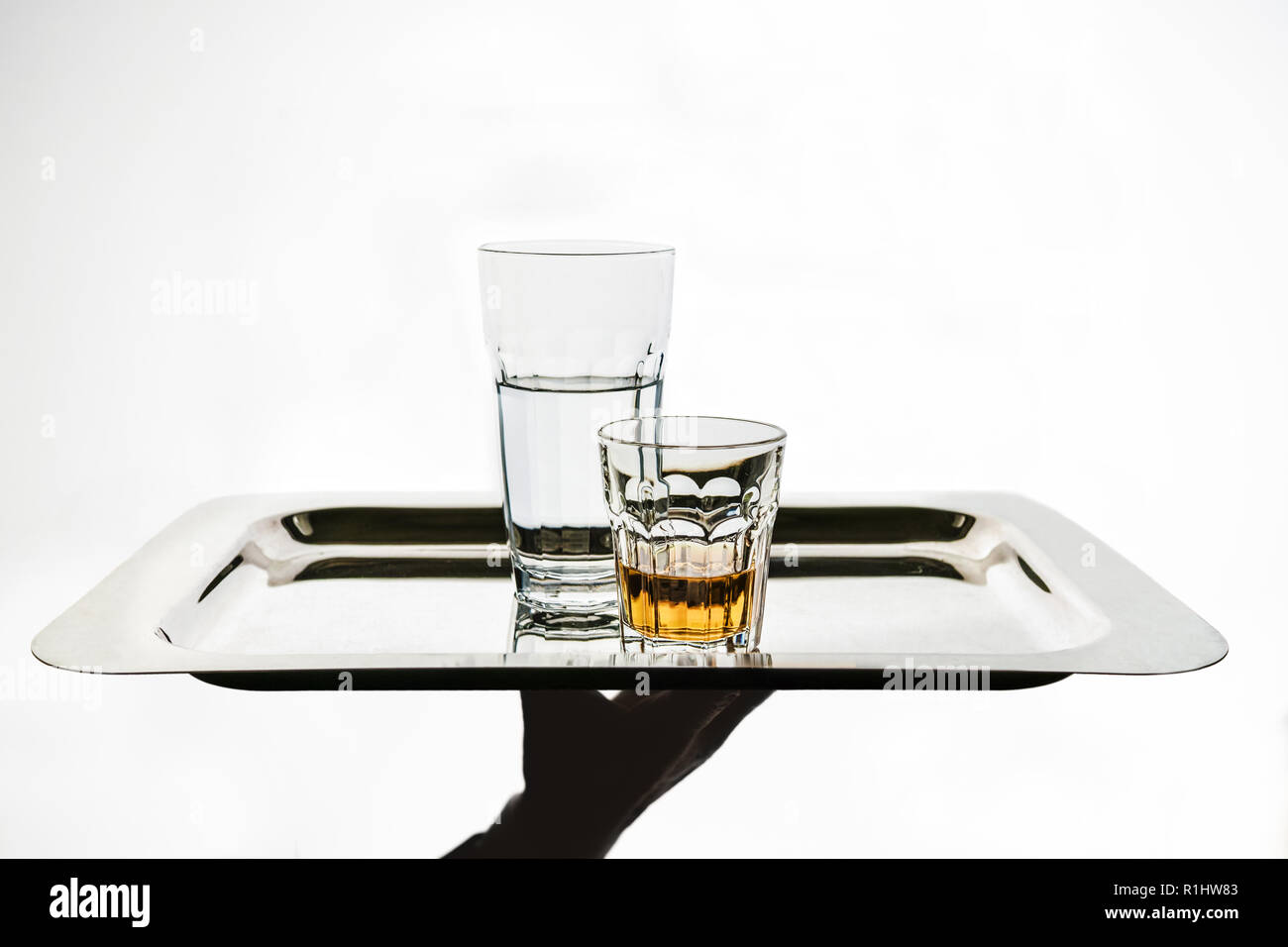 Die Kellnerhand bringt auf eine silberne Platte, ein Glas Wasser und ein Glas Alkohol. Isolierter Kopierbereich. Stockfoto