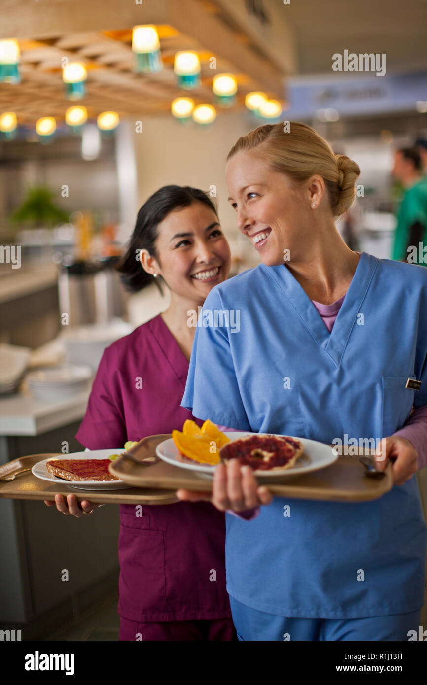Zwei junge Krankenschwestern Lächeln und miteinander chatten, während Sie Ihr Mittagessen aus dem Krankenhaus Kantine erhalten. Stockfoto