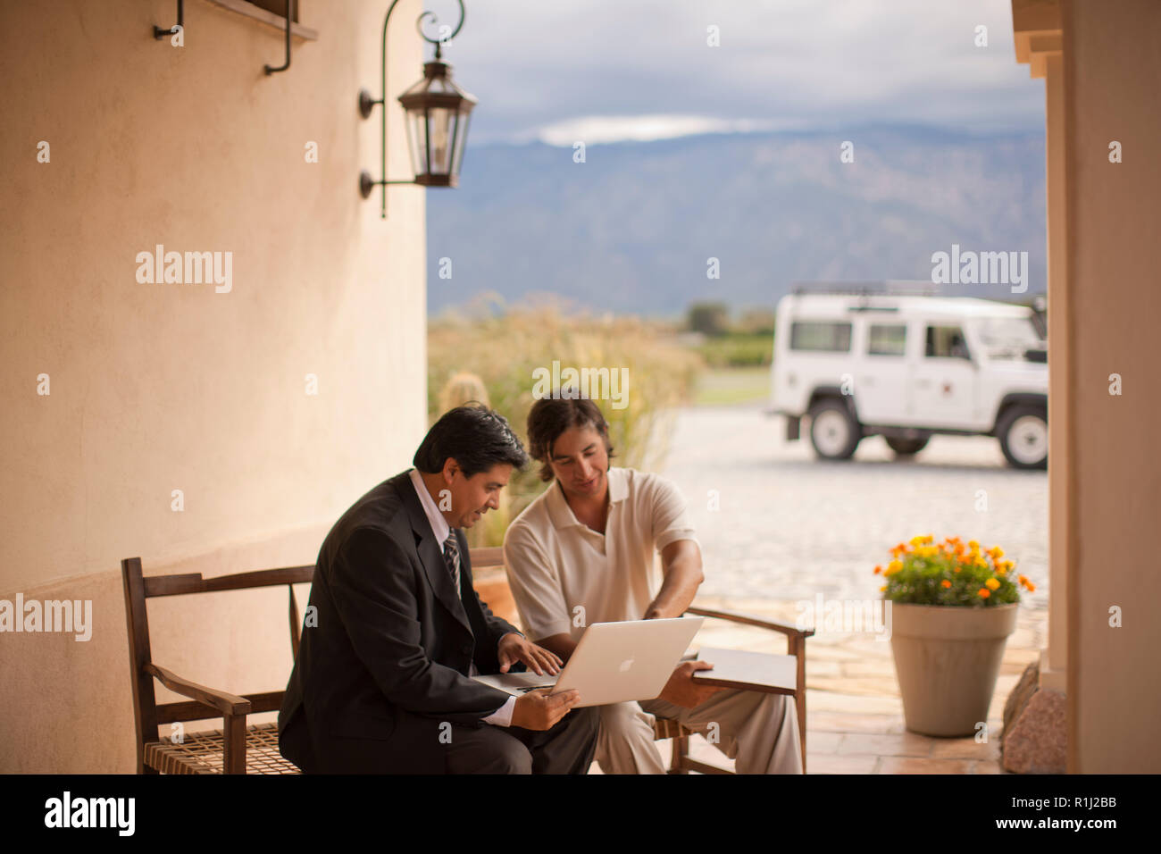 Zwei mittig - erwachsene Männer an einem Laptop schauen, während sie nebeneinander auf einer Veranda sitzen. Stockfoto