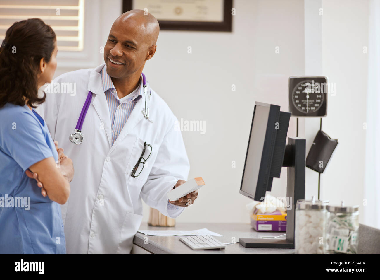 Lächelnd männlicher Arzt ein Gespräch mit einem weiblichen Krankenschwester über eine Box der Medikation in seinem Büro. Stockfoto