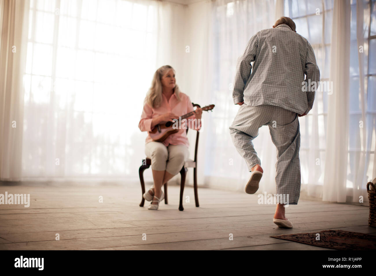 Ältere Menschen tanzen, während seine Frau eine Gitarre spielt. Stockfoto