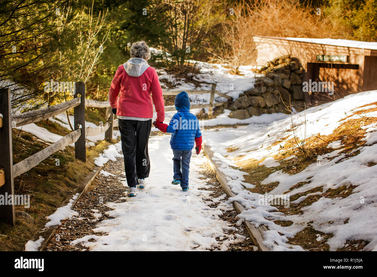 Großmutter und Enkel gingen Hand in Hand an einem verschneiten Fußweg. Stockfoto