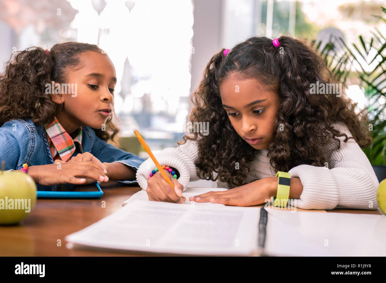 Curly Schulmädchen tragen gelbe smart Watch machen ihre Hausaufgaben Stockfoto