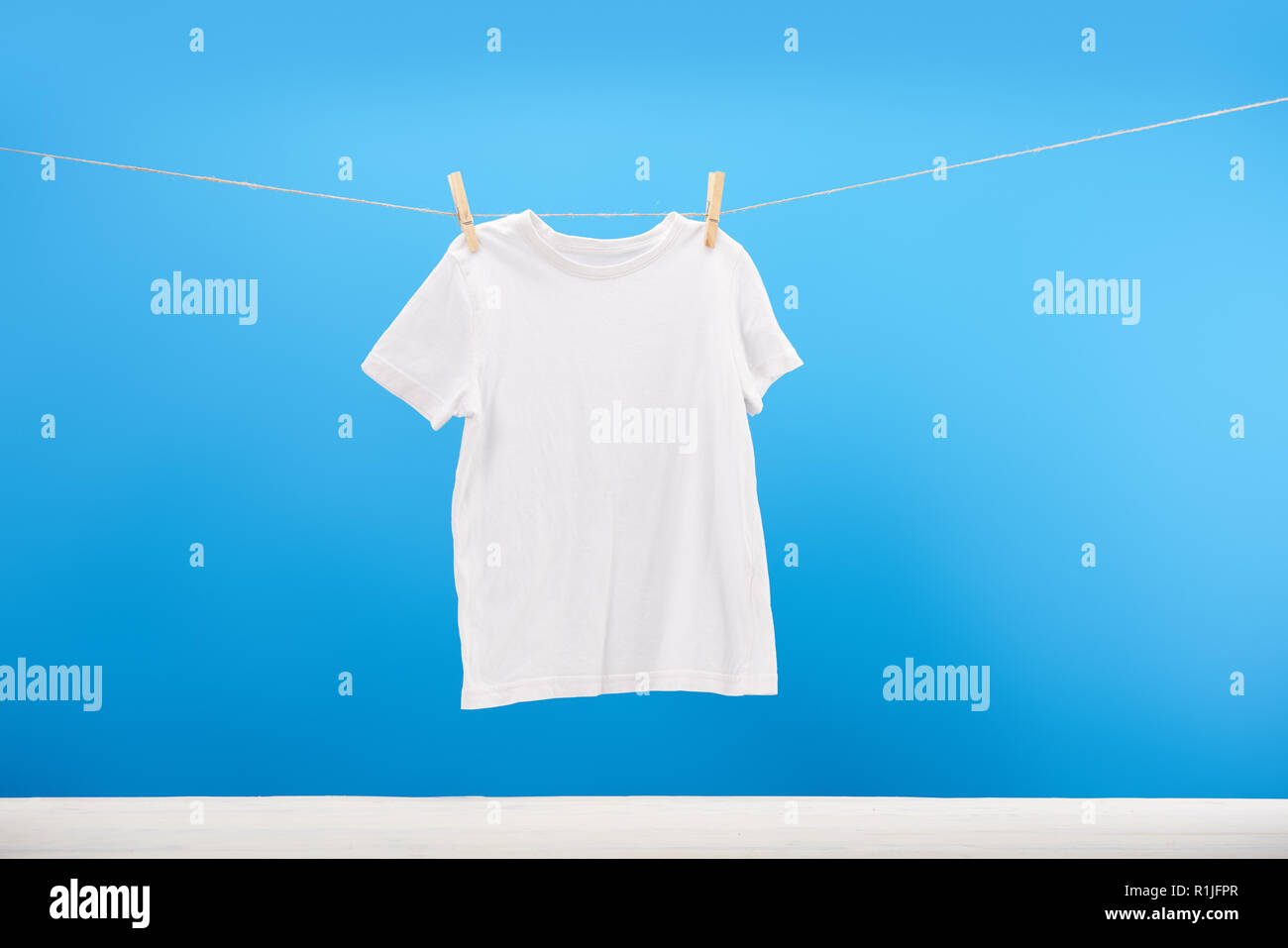 Sauberes weißes T-Shirt hängen auf wäscheleine auf Blau Stockfoto