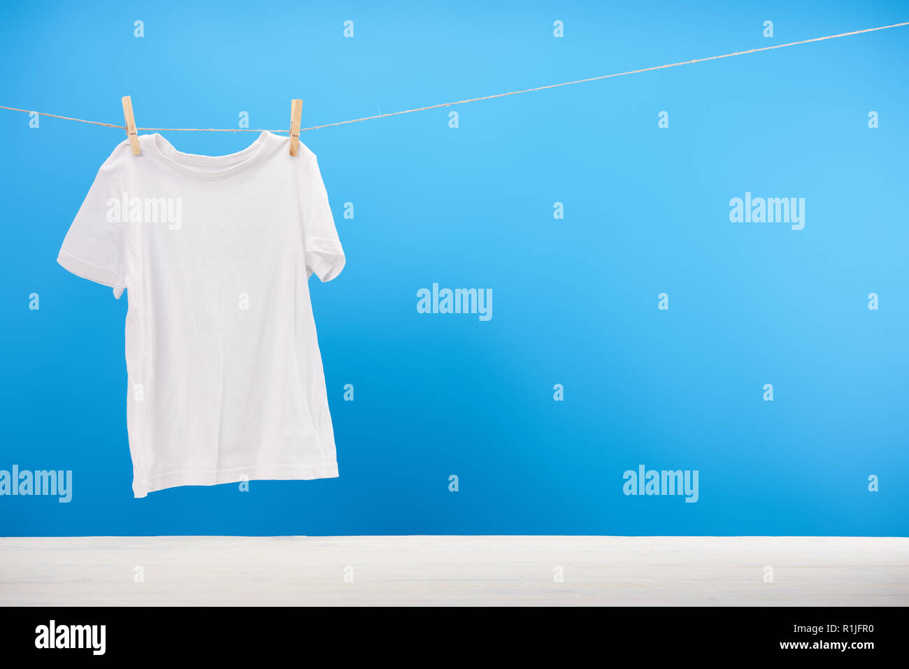 Sauberes weißes T-Shirt hängen am Seil auf Blau Stockfoto
