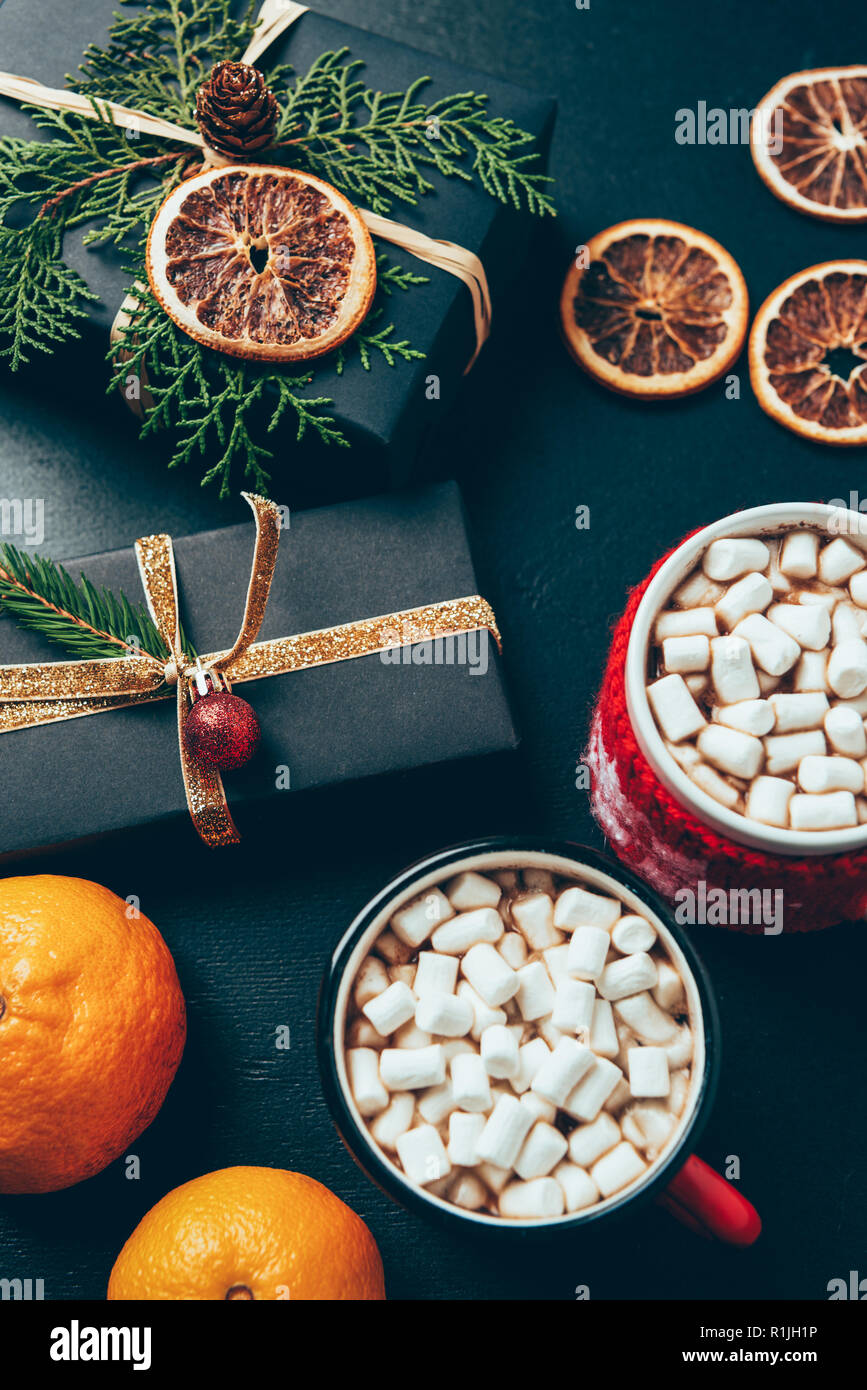 Blick von oben auf die Tassen heiße Getränke mit Marshmallows, Mandarinen und Weihnachten präsentiert sich auf der schwarzen Oberfläche Stockfoto