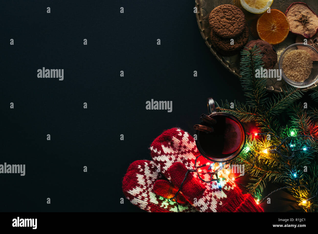 Blick von oben auf die Tasse Glühwein, Garland, Fäustlinge und Cookies auf schwarz, Weihnachten Konzept isoliert Stockfoto