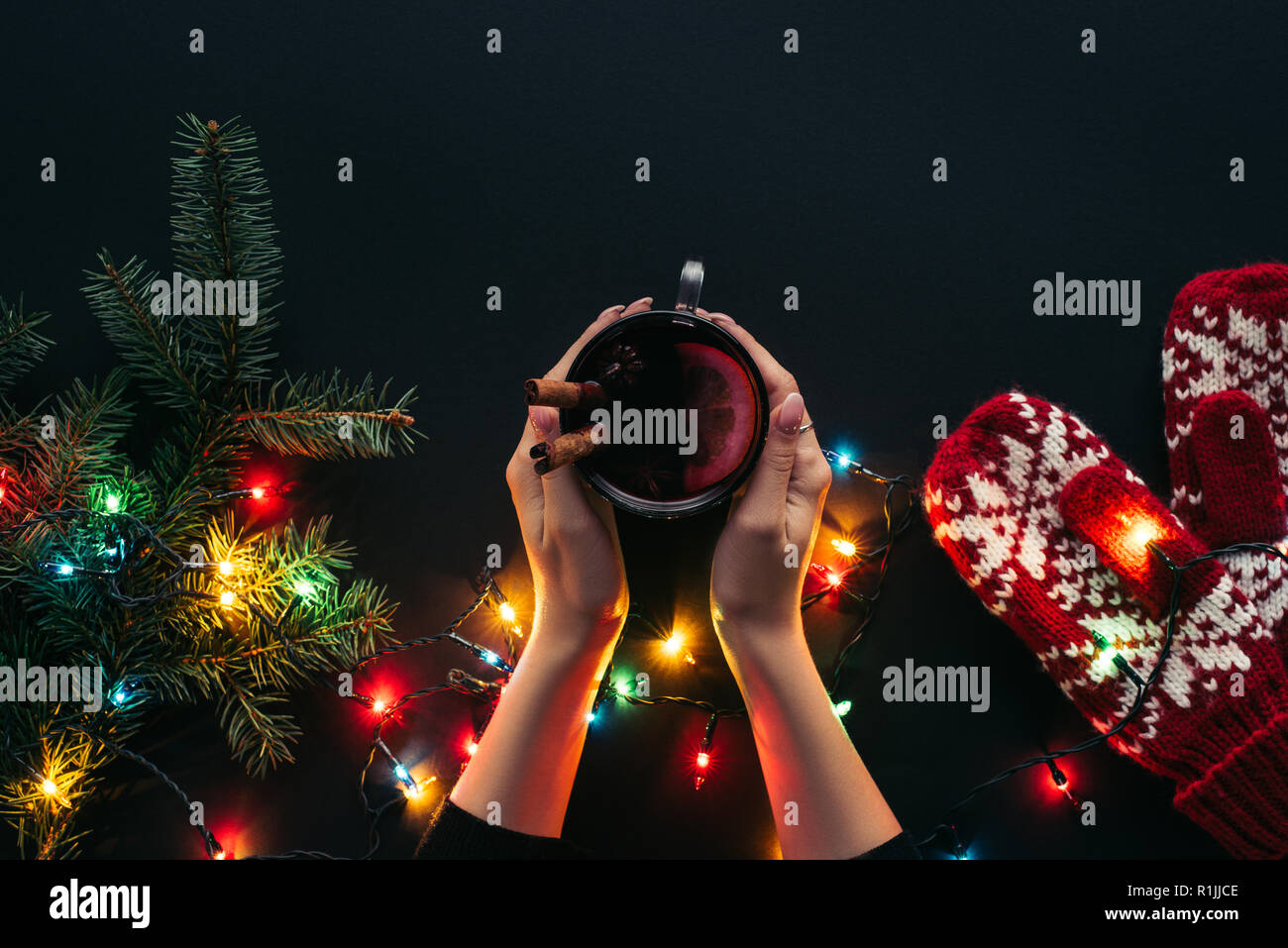 Zugeschnittenes Bild der Frau mit Glühwein in der Nähe von Weihnachten Girlande isoliert auf Schwarz Stockfoto