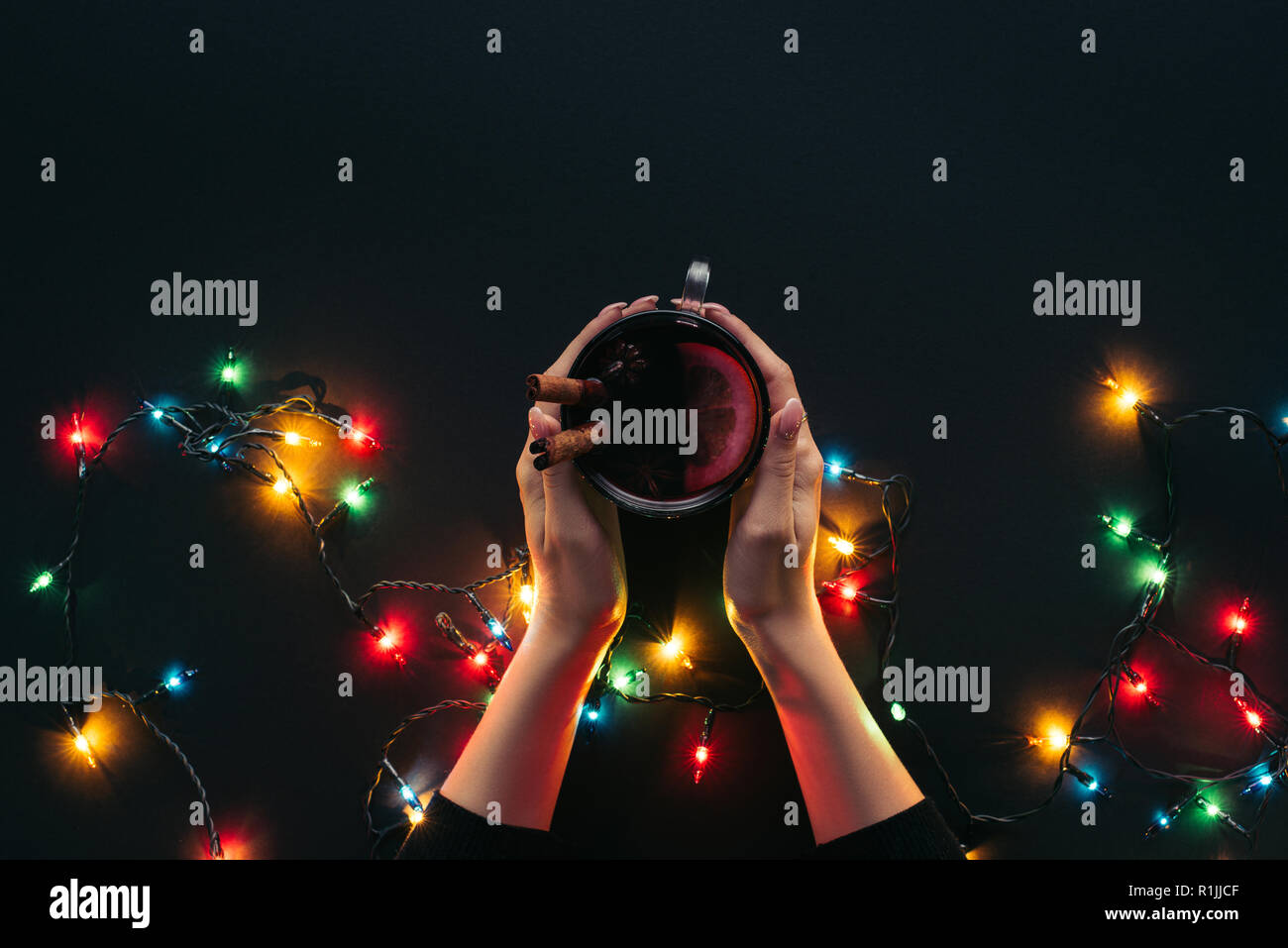 Zugeschnittenes Bild der Frau mit Glühwein in der Nähe von Garland auf schwarz, Weihnachten Konzept isoliert Stockfoto