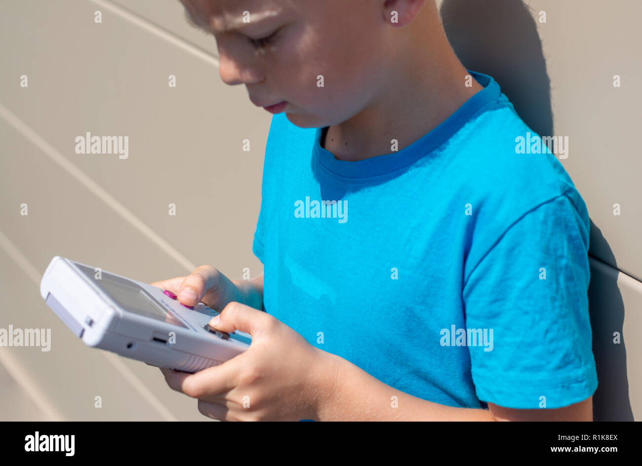 Junge mit seinem Nintendo Gameboy Computerspiele zu spielen. 90er Jahre Ambiente. Im Freien einstellen. Stockfoto
