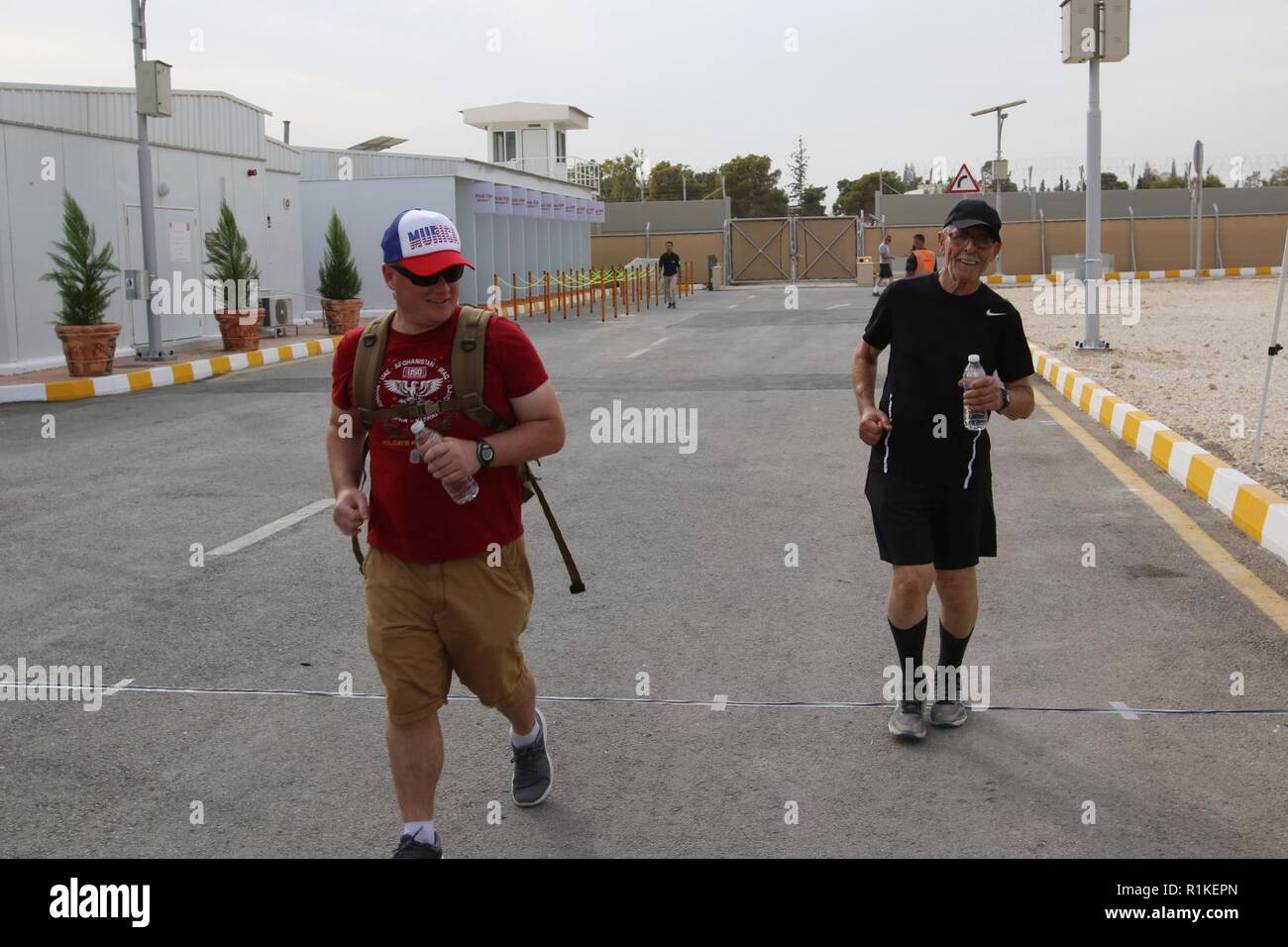 AMMAN, Jordanien - 82-jährige Abdul Wahid al Rubaye (rechts) überquert die Ziellinie der 28-Meilen-Marsch für die Fallen-Jordan Veranstaltung Okt. 6, 2018. Sgt. Timothy James (links) ein Arzt mit der 1. Staffel, 18 Cavalry Regiment, 79th Infantry Brigade Combat Team, Kalifornien Nationalgarde, gingen dann die letzten 11 km mit Rubaye als Sicherheitsmaßnahme. Die Veranstaltung im gemeinsamen Training Center war ein Schatten März des 7. jährlichen 28 Infanterie Division MFTF Sept. 29 am Fort Indiantown Gap, Pennsylvania statt. Stockfoto