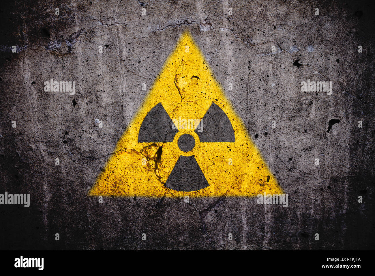 Radioaktiven (Atomkern ionisierende Strahlung) Gefahr Warnung Symbol in dreieckige gelbe Form auf einem massiven gerissenen Beton Zement Wand wit lackiert Stockfoto