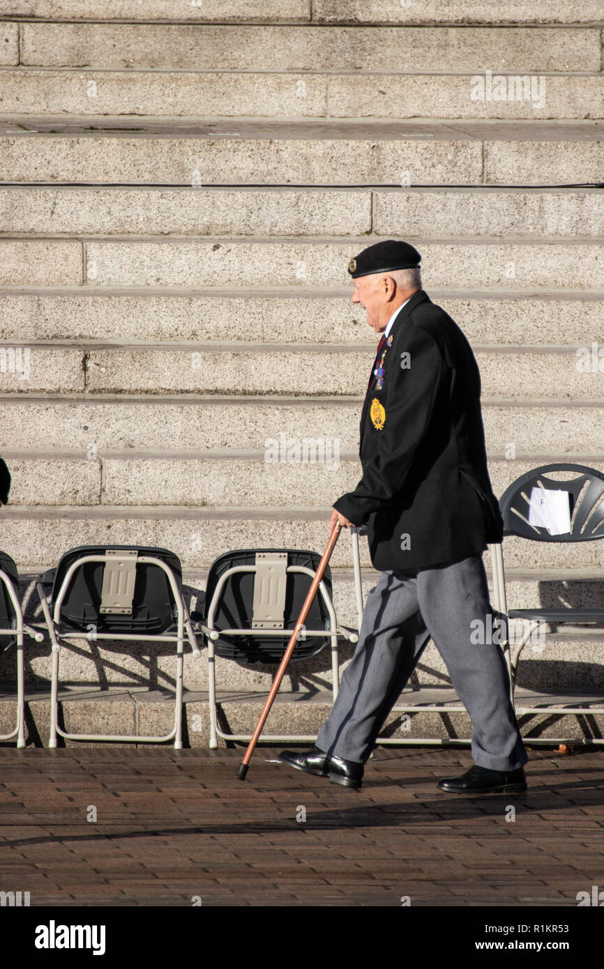 Eine ältere britische Kriegsveteran seine Medaillen und Baskenmütze mit seinen Spazierstock seinen Platz für einen Tag der Erinnerung Parade zu nehmen tragen Stockfoto