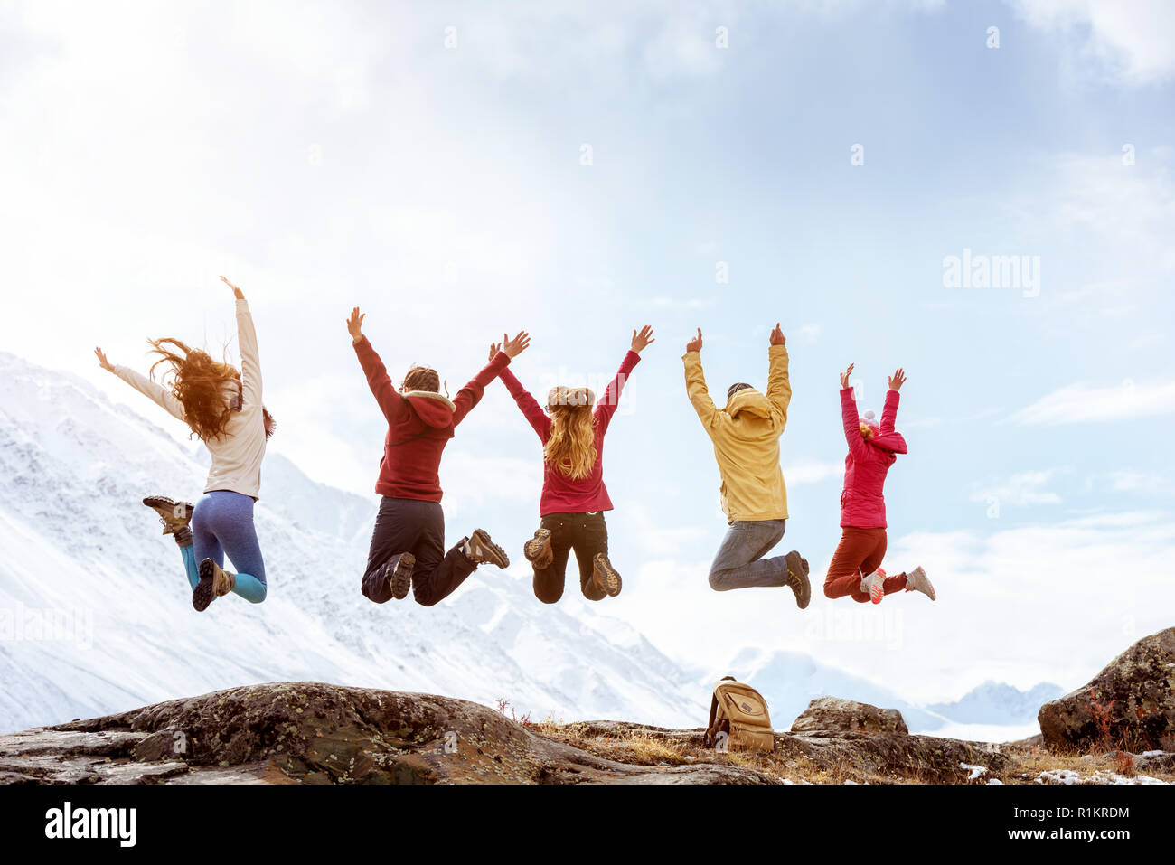 Gruppe von fünf glückliche Freunde springt auf dem Felsen auf dem Hintergrund der schneebedeckten Berge Stockfoto