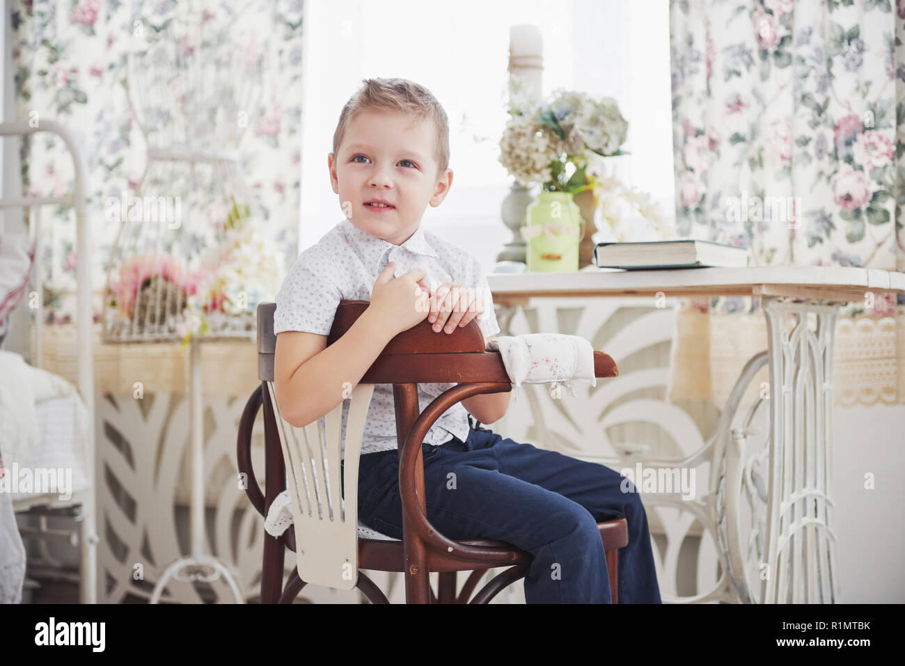 Kleiner Junge in blau Hose Jeans sitzt auf dem hölzernen Stuhl im Zimmer.  Macht Hausaufgaben. Zurück zur Schule Stockfotografie - Alamy