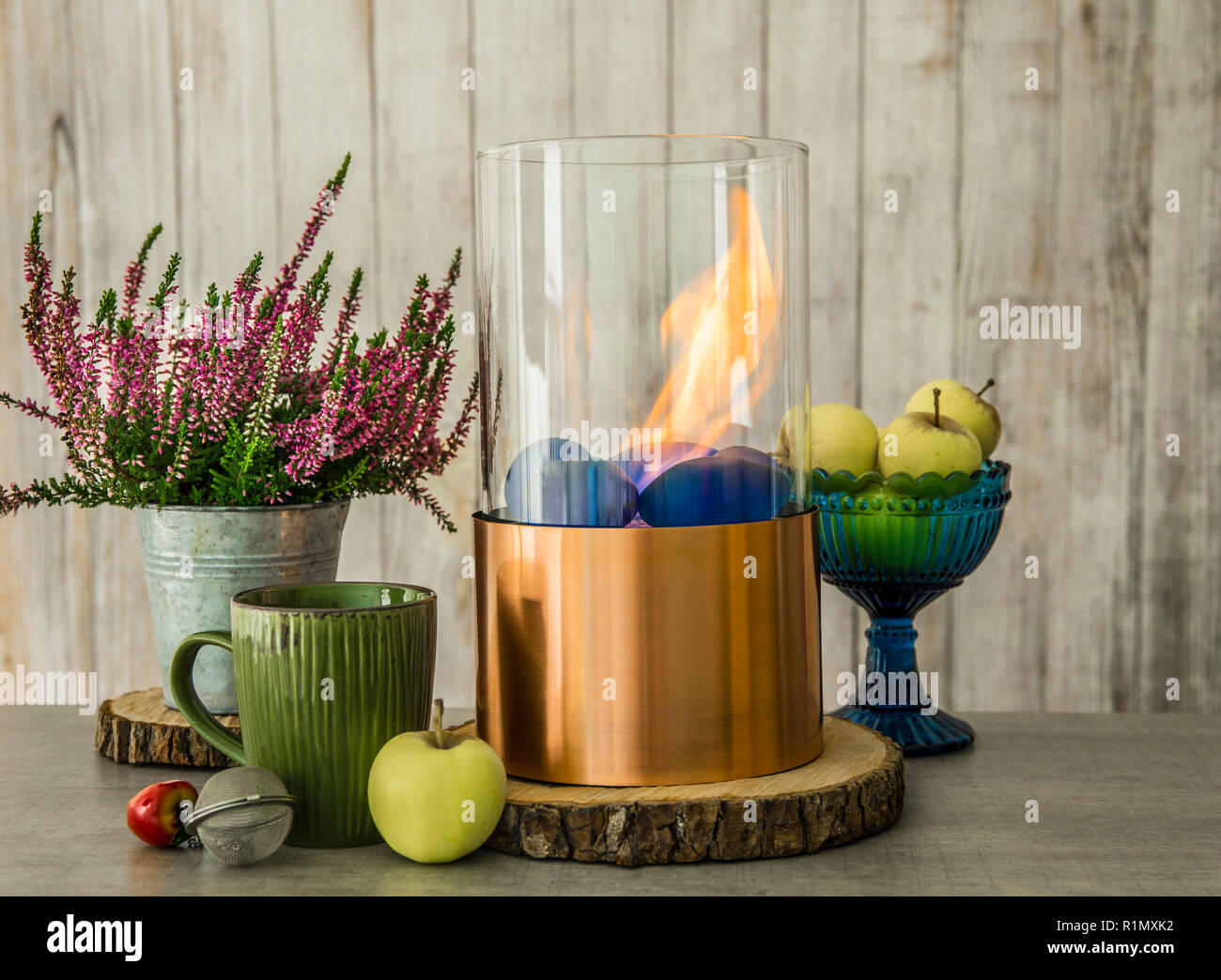 Freistehende portable Glas und Kupfer Metall brennenden Kamin Bio Ethanol  Gas auf Holztisch mit T-Stück Schale, blaue Schale mit grünen Äpfeln.  Herbst set c Stockfotografie - Alamy