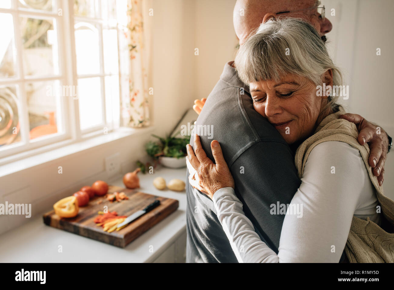 Seitenansicht eines älteren Paares einander zu Hause umarmte. Ältere Frau ihren Ehemann mit geschlossenen Augen stehen in der Küche. Stockfoto