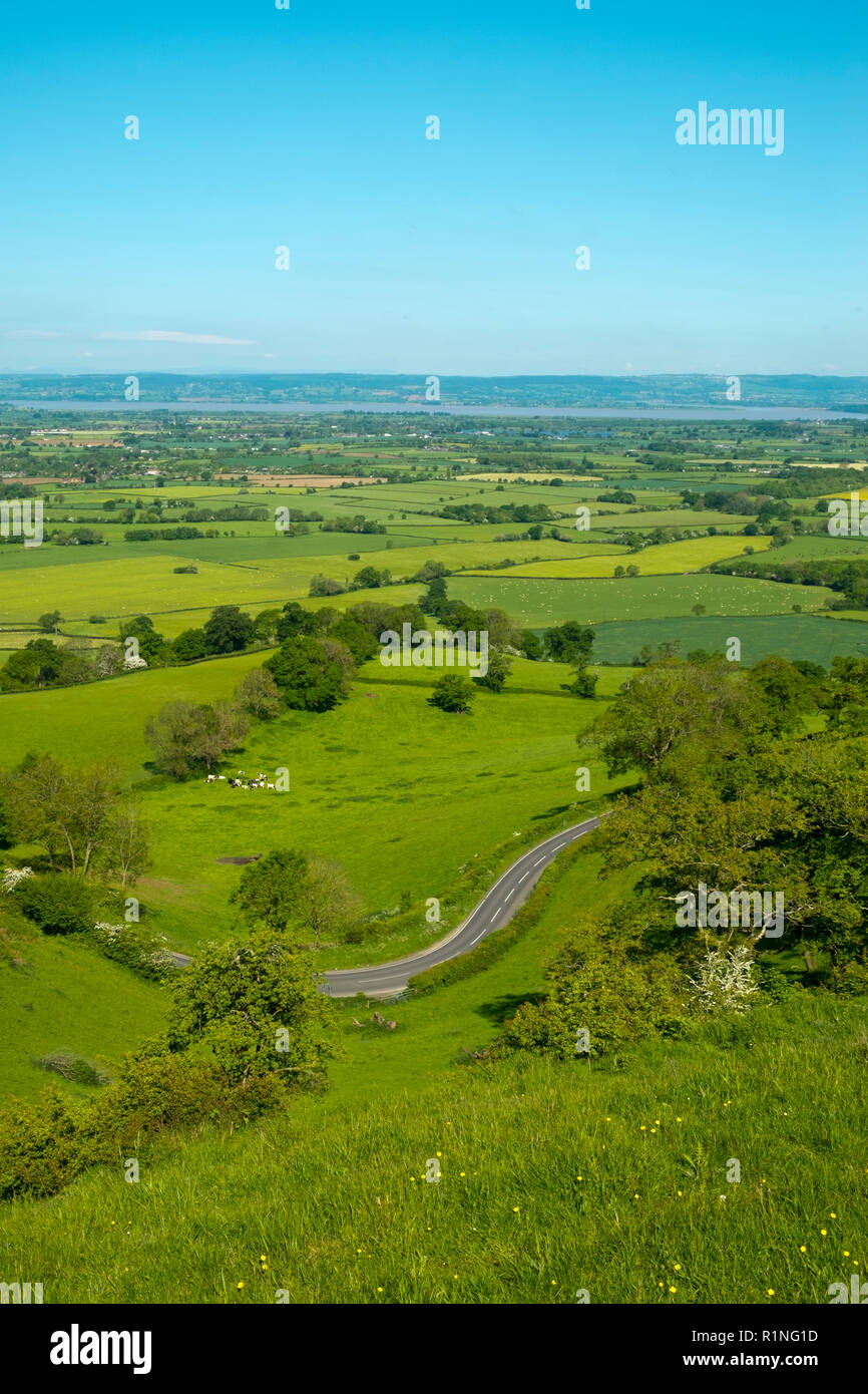 Umfangreiche Blick in Richtung des Flusses Severn und den Wald von Dean über einen Flickenteppich aus Feldern mit einer kurvenreichen Straße im Vordergrund, Coaley Peak Picknickplatz und Aussichtspunkt, Gloucestershire, VEREINIGTES KÖNIGREICH Stockfoto