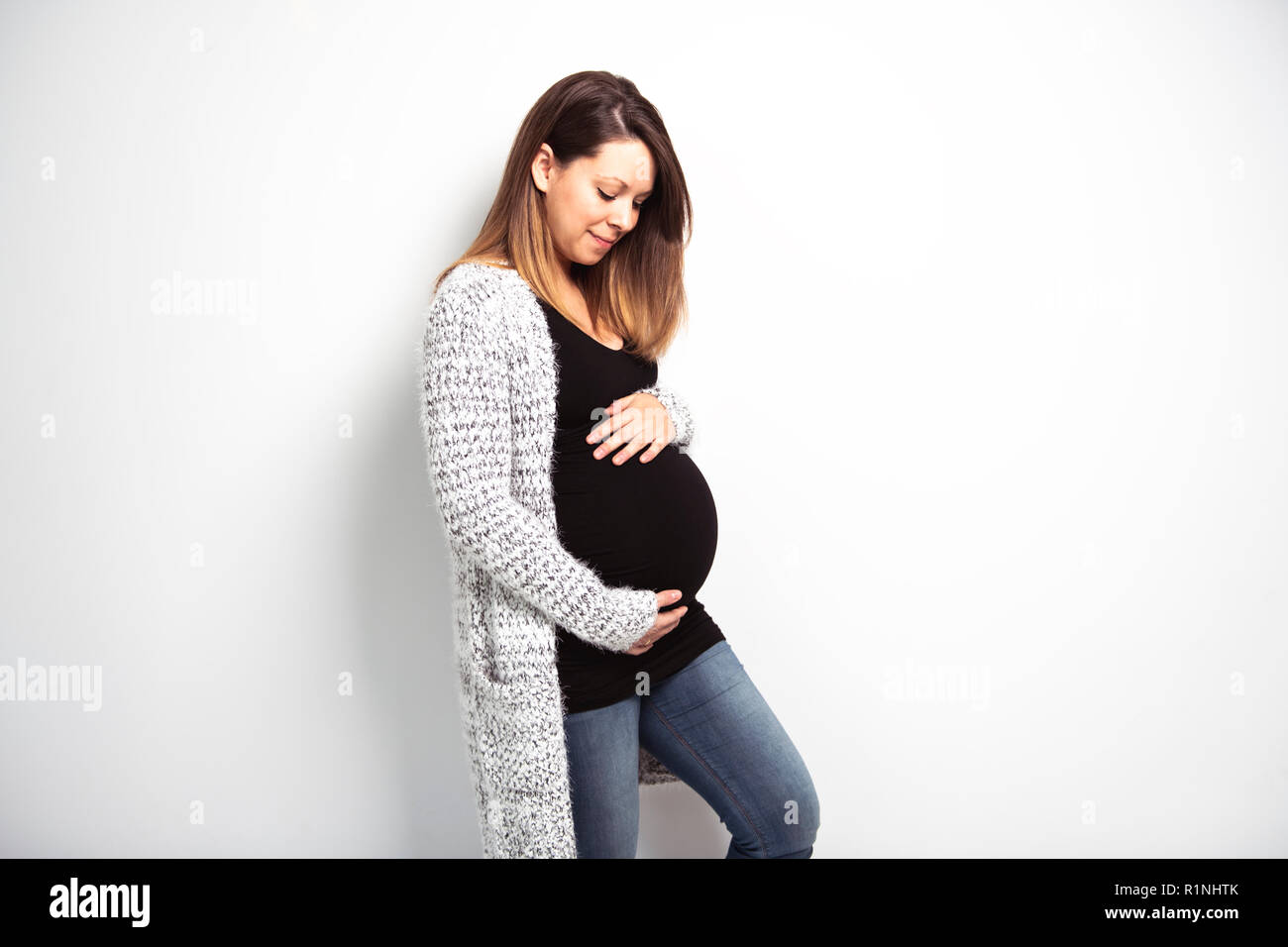 Ein Porträt der Glückliche schwangere Frau mit Händen auf Magen auf weißem Hintergrund Stockfoto