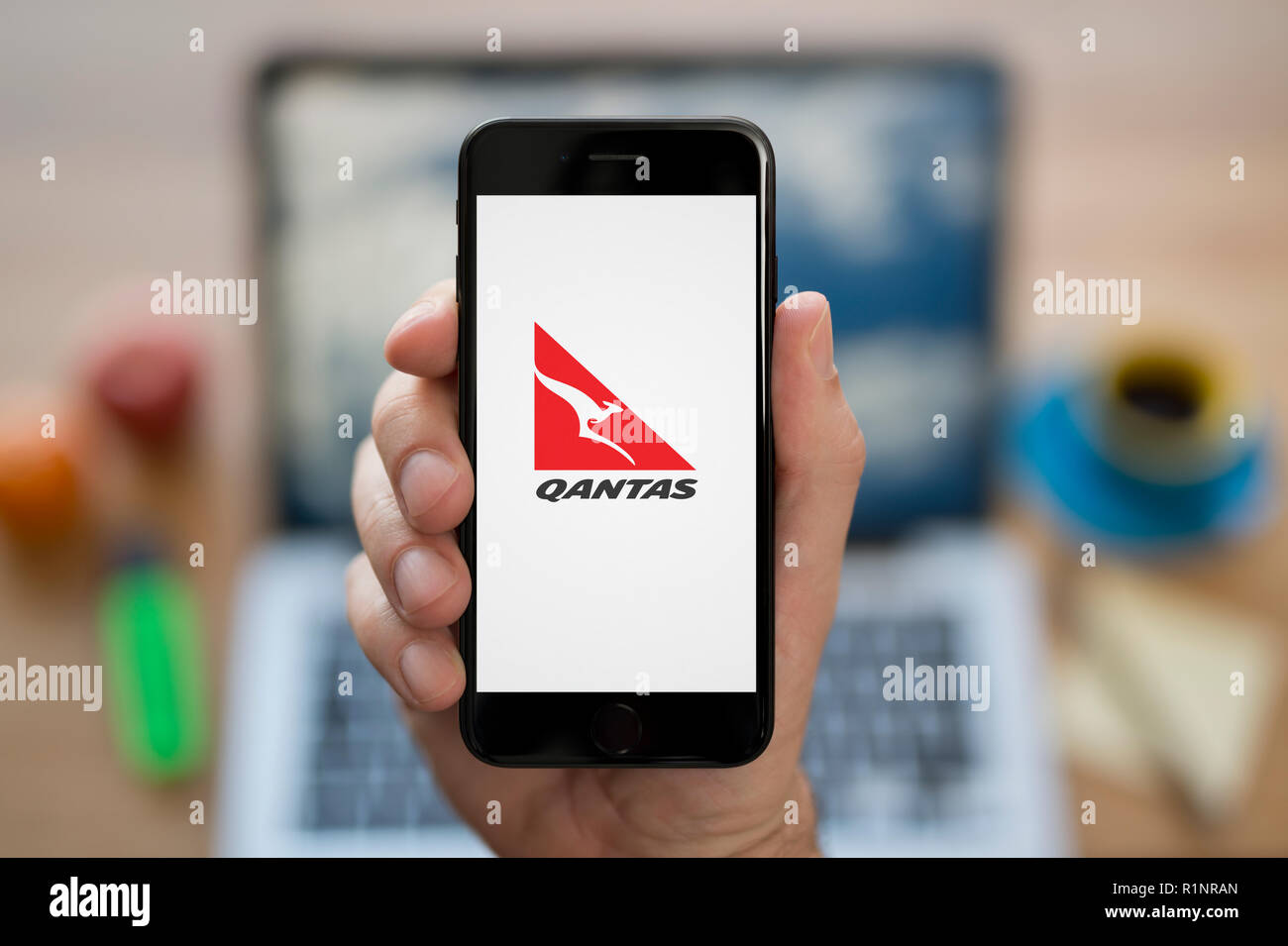 Ein Mann schaut auf seinem iPhone die zeigt die Qantas logo, während saß an seinem Computer Schreibtisch (nur redaktionelle Nutzung). Stockfoto