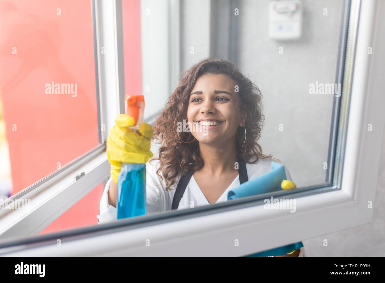 Schöne junge Frau wird mit einem Staubwedel und ein Spray, Kamera und lächelnd, während Windows Reinigung im Haus Stockfoto