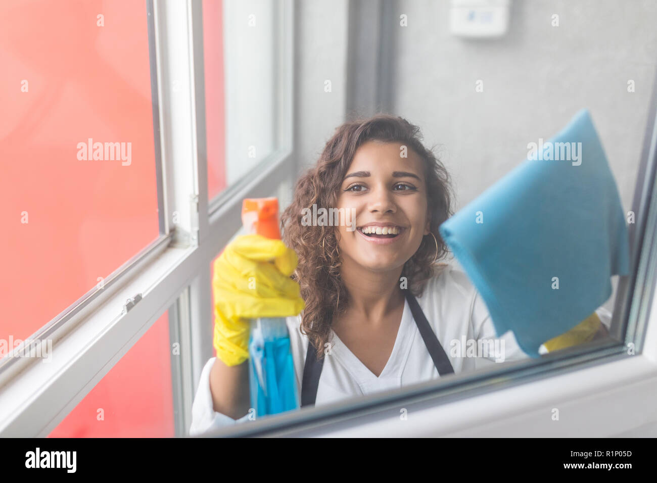 Schöne junge Frau wird mit einem Staubwedel und ein Spray, Kamera und lächelnd, während Windows Reinigung im Haus Stockfoto