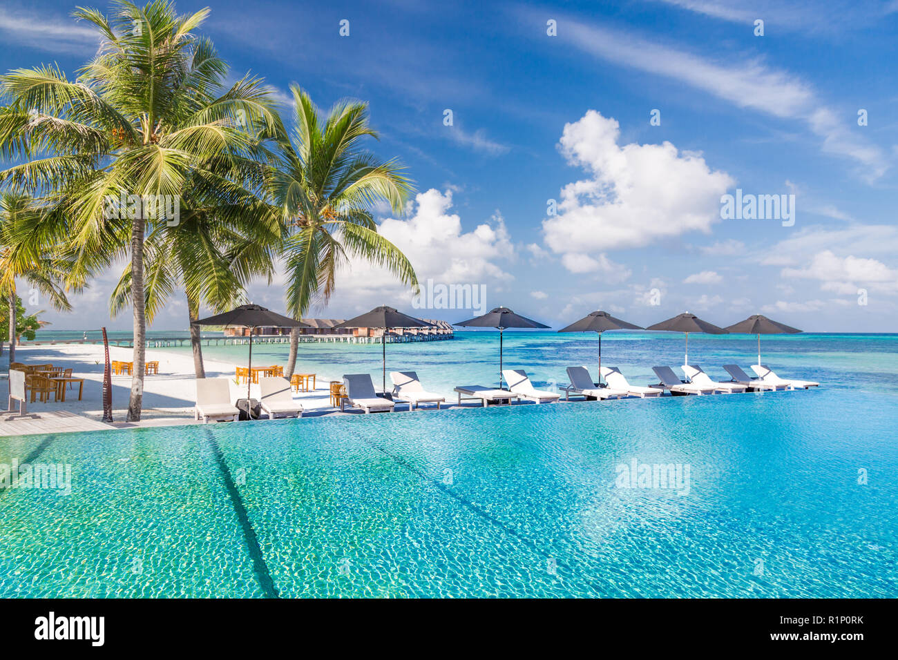 Liegestühle und Infinity Pool über fantastische tropische Lagune. Luxus und Urlaub Konzept Stockfoto
