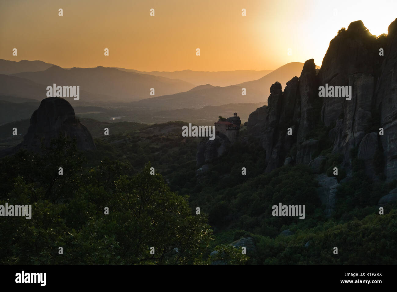 Die riesigen Felsen mit den Klöstern und Sonnenuntergang hinter die Berge in der Ferne in Meteora, Thessalien, Griechenland Stockfoto