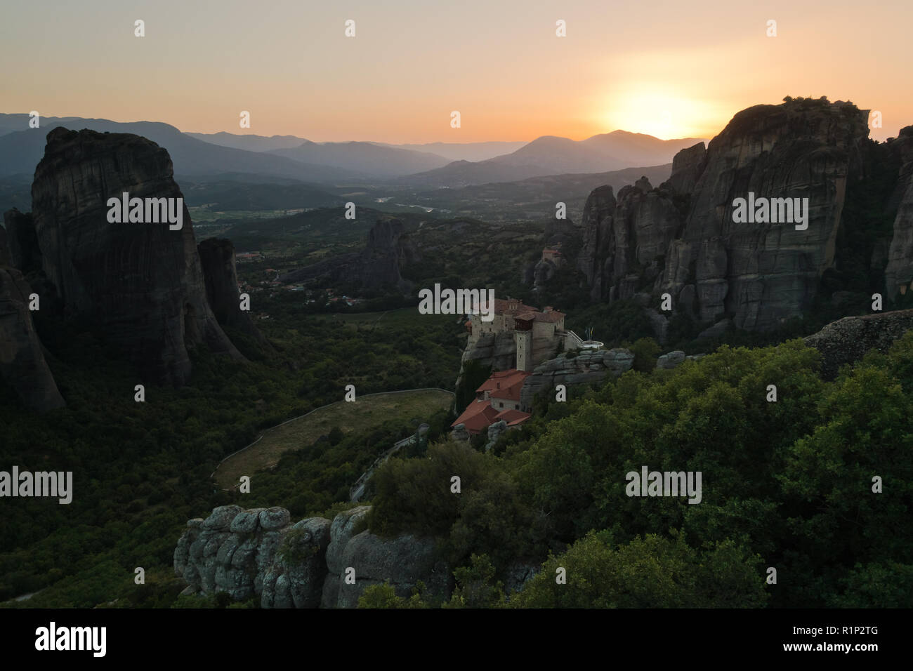 Die riesigen Felsen mit den Klöstern und Sonnenuntergang hinter die Berge in der Ferne in Meteora, Thessalien, Griechenland Stockfoto
