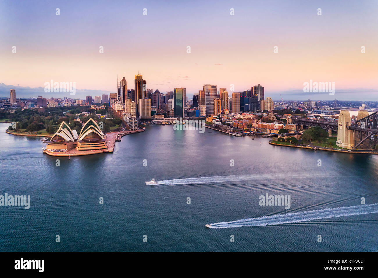 Zwei schnelle Boote auf dem ruhigen Wasser des Hafens von Sydney mit Blick auf den Circular Quay und Innenstadt hoch aufragenden Türmen und australischen Wahrzeichen bei Sonnenaufgang mit Rosa Stockfoto