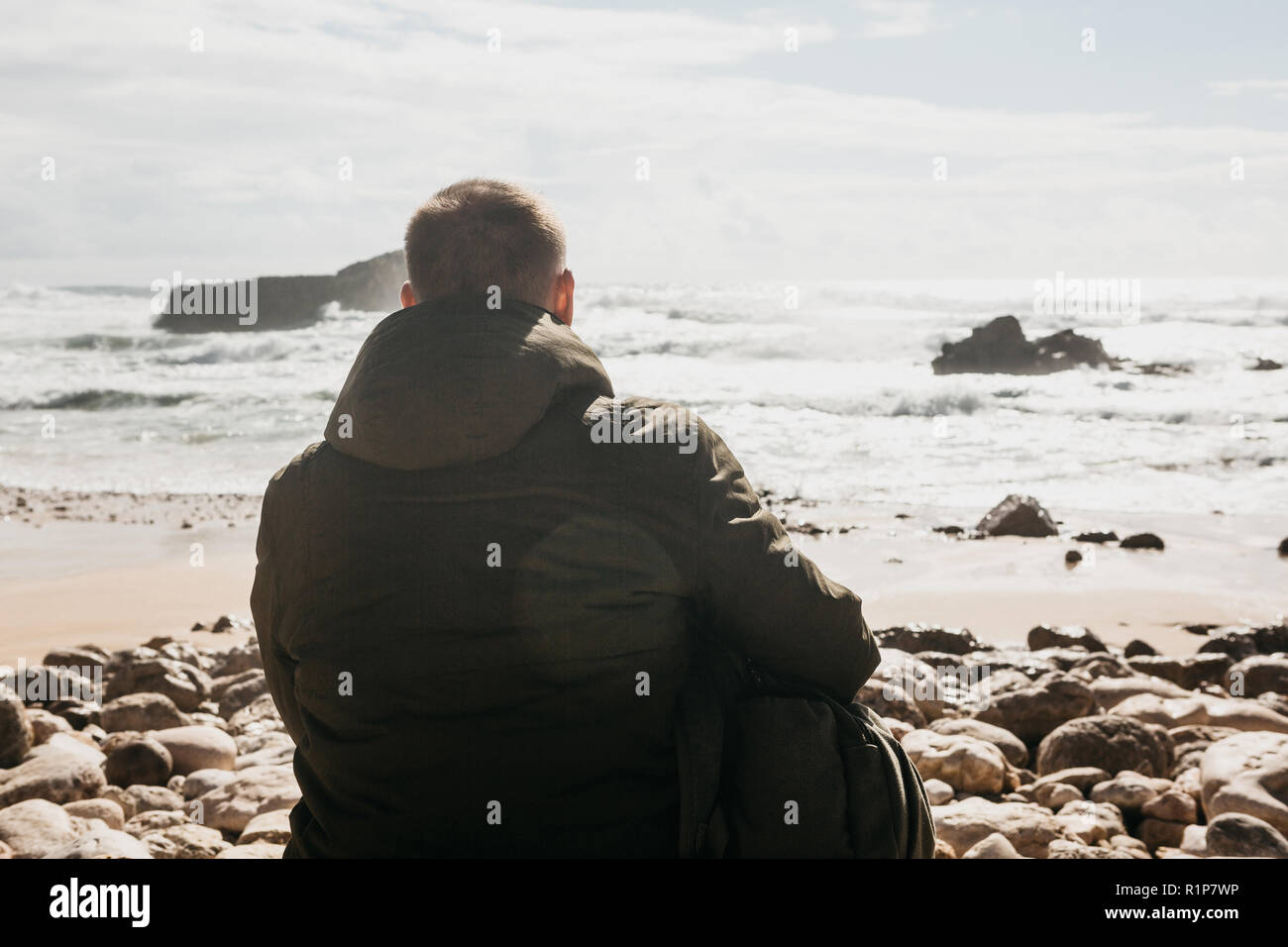 Ein Mann mit einem Rucksack oder ein Tourist oder ein Reisender in der Einsamkeit bewundert einen schönen Blick auf den Atlantik in Portugal. Suche nach Seele oder die Einheit mit der Natur. Stockfoto