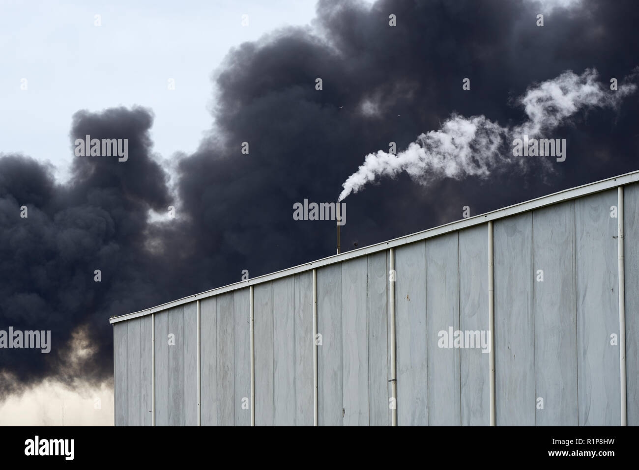 Giftiger Rauch von einem Westen Footscray Brand am 30. August 2018 können gesehen werden brüllend hinter eine moderne Lagerhalle mit kontrastierenden weißen Dampf. Stockfoto