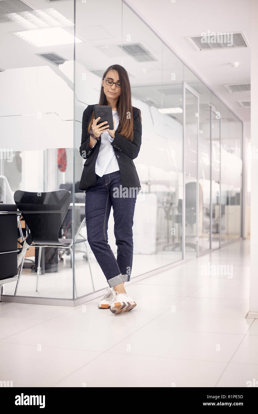 Eine junge Frau, weiße Arbeiter, die ihre Arbeit über Tablet. voller Länge geschossen, im modernen Innenraum Büro Platz. Stockfoto