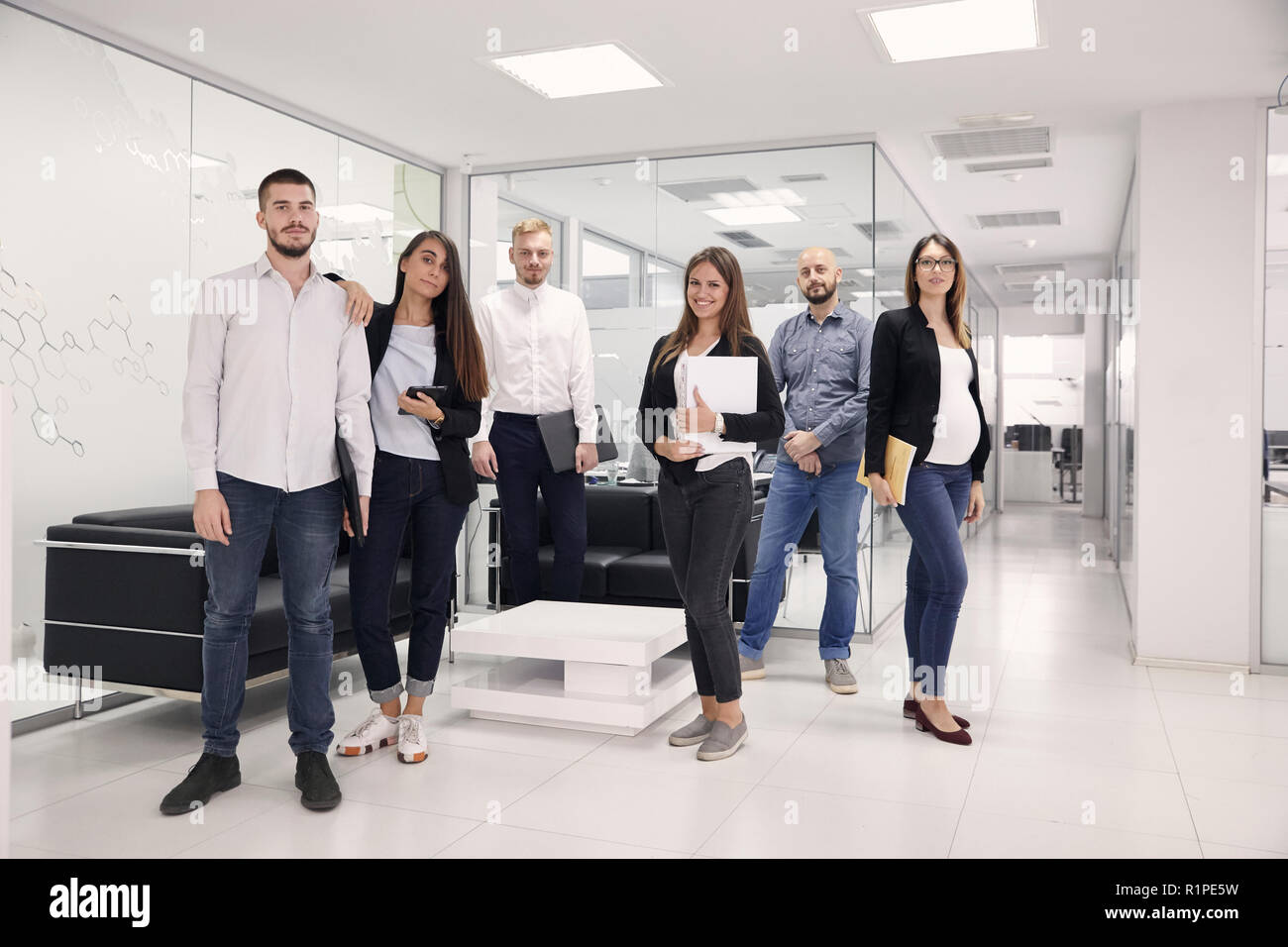 Gruppe von sechs Personen posieren, an der Kamera suchen, 20-29 Jahre und 30-39 Jahre alt, der verschiedenen Angestellte, gekleidet 'Smart casual'. moderne Büro Stockfoto