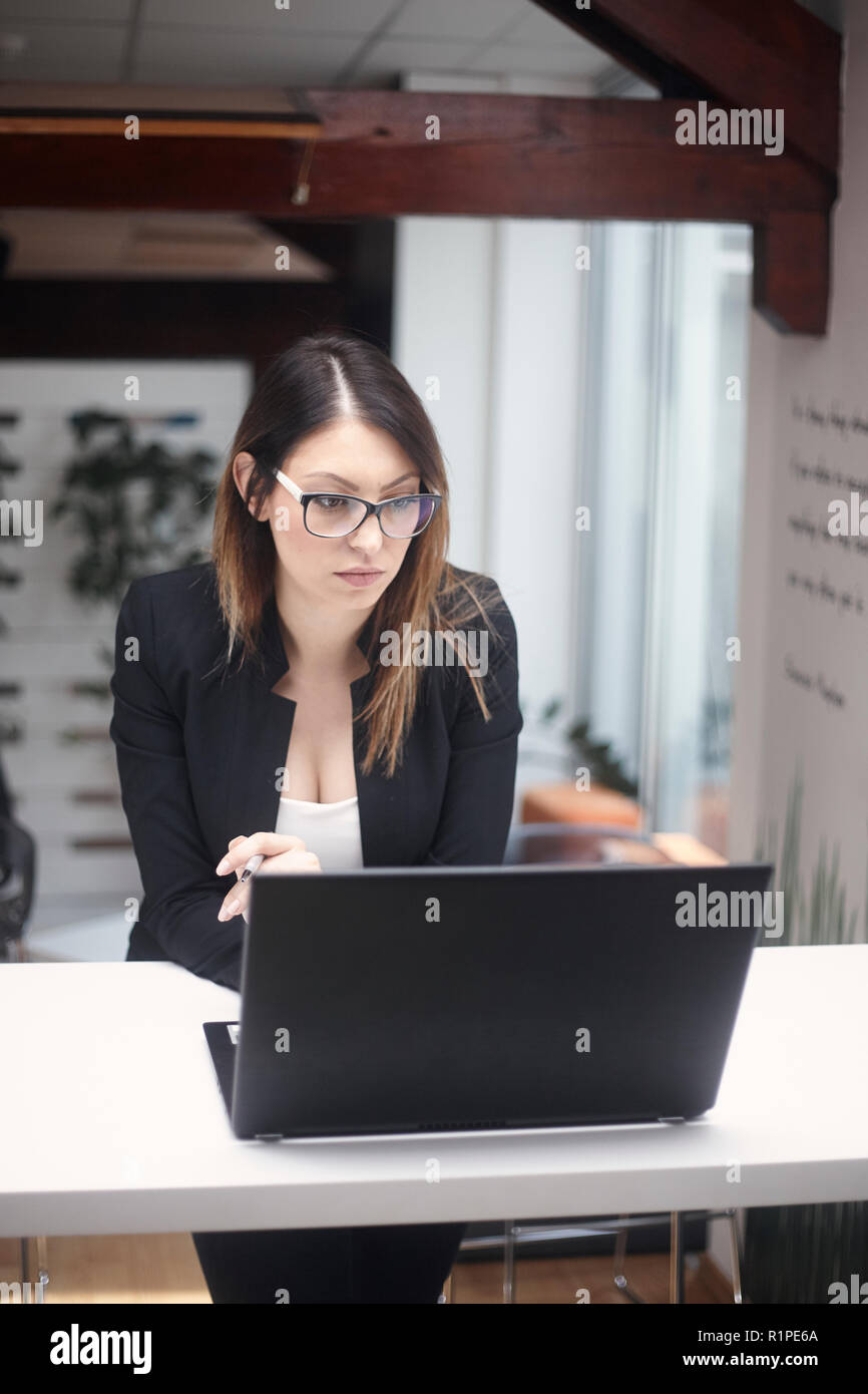 Eine junge Frau denken, 30-39 Jahre alt, obere Körper geschossen. Arbeiten am Laptop im Büro. Stockfoto