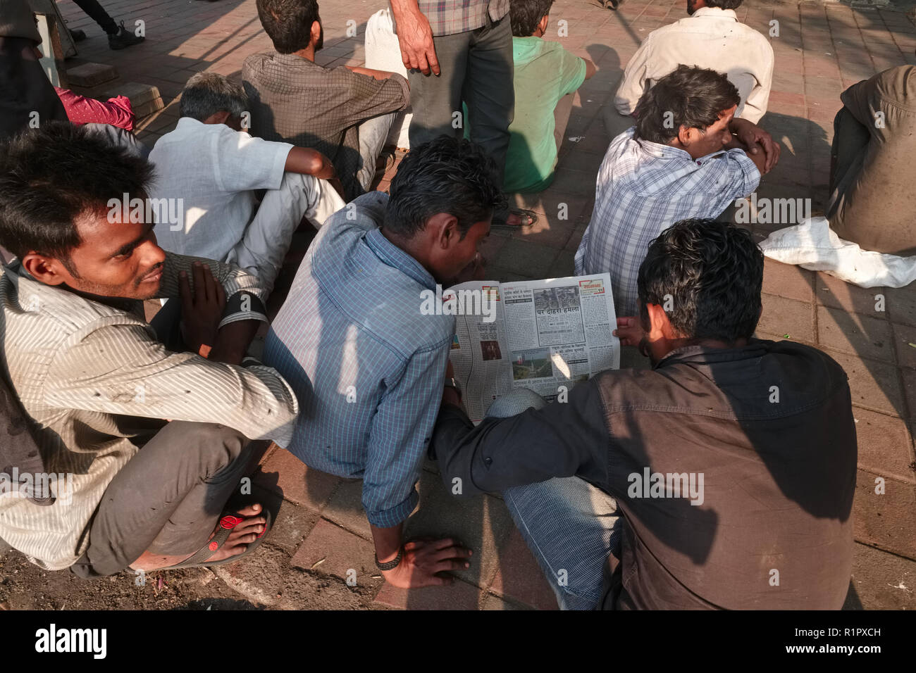 Arme Bewohner von Mumbai, Indien, auf einem Fußweg warten auf Essen Handzettel eingesetzt, einige, die Zeit eine Zeitung lesen Stockfoto