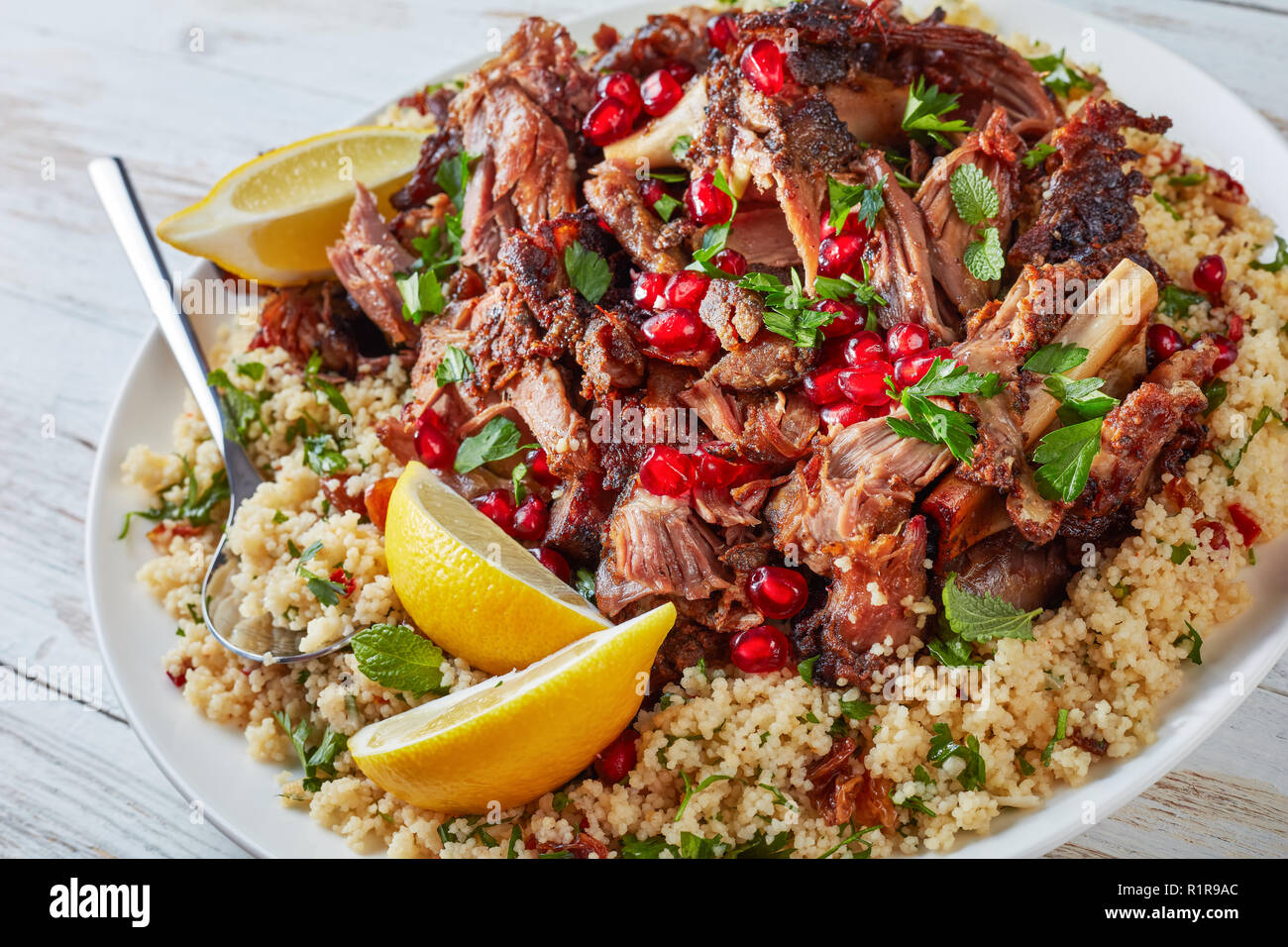 Couscous salat Petersilie garniert mit langsam Braten zartes Fleisch fallen aparr, bestreut mit Granatapfel Samen auf einem weißen Teller mit Löffel, von oben betrachten, Stockfoto