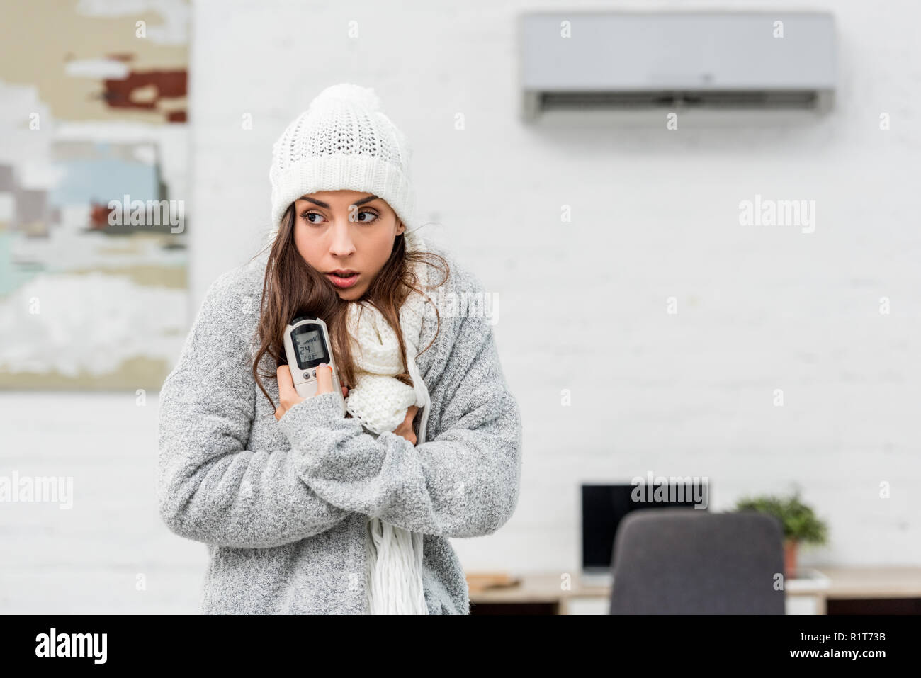 Einfrieren junge Frau in warme Kleidung holding Fernbedienung mit Klimaanlage auf Hintergrund Stockfoto
