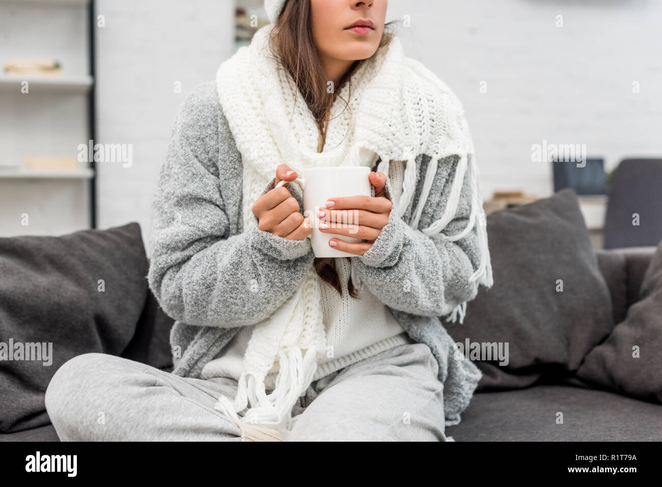 Aufnahme des Kranken jungen Frau in warme Kleidung holding Tasse heißes Getränk beim Sitzen auf der Couch zu Hause 7/8 Stockfoto