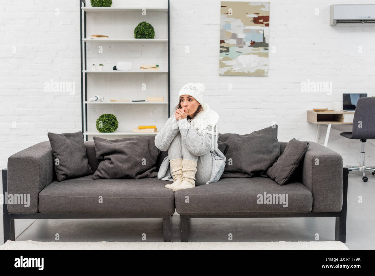 Zugefrorene junge Frau in warme Kleidung auf dem Sofa zu Hause sitzen Stockfoto
