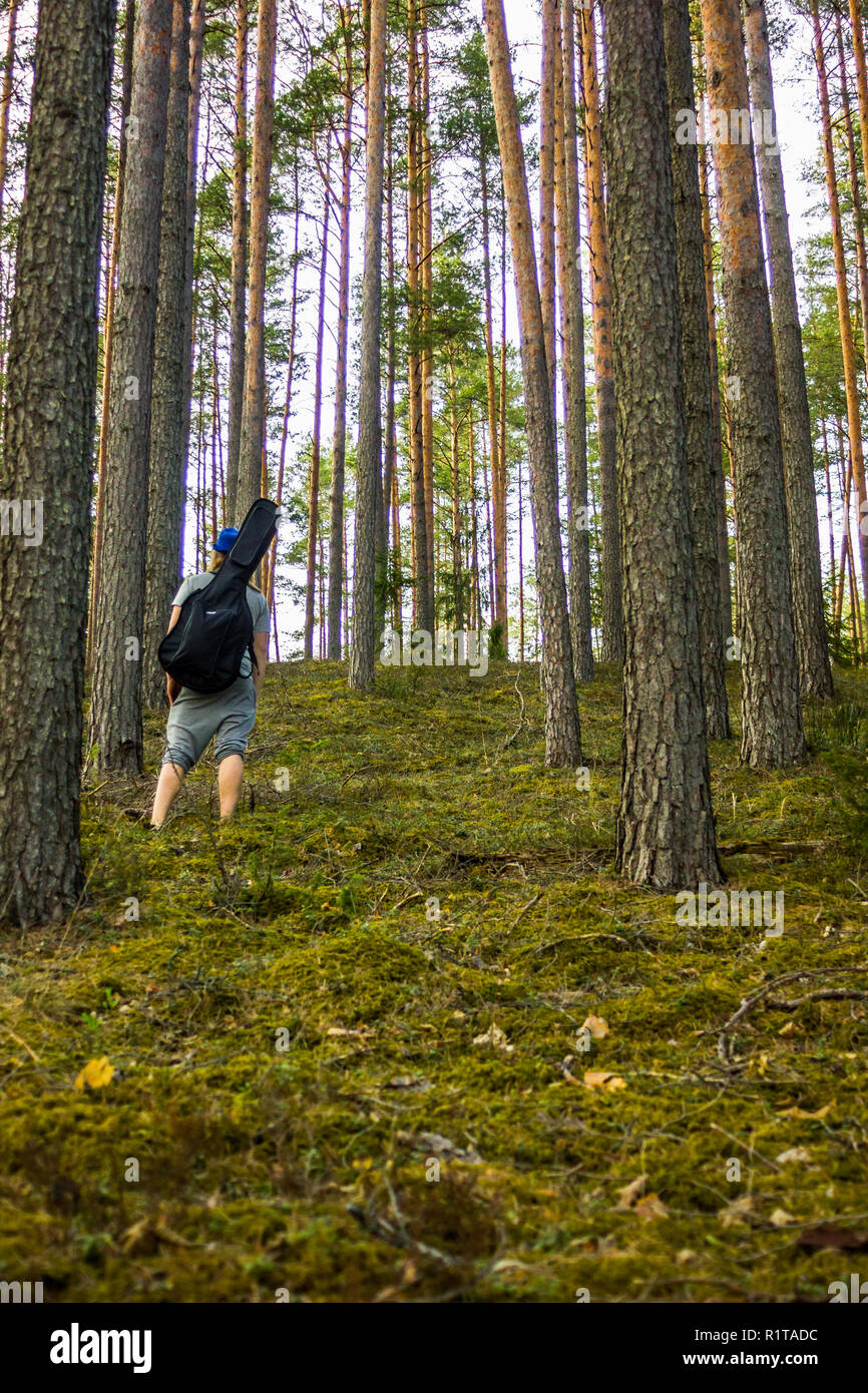 Jung und hübscher Kerl im Wald mit einer Gitarre auf seinen Schultern und blauen Hut auf dem Kopf auf einem sonnigen Frühling Tag - Moody Foto mit einem Co Stockfoto