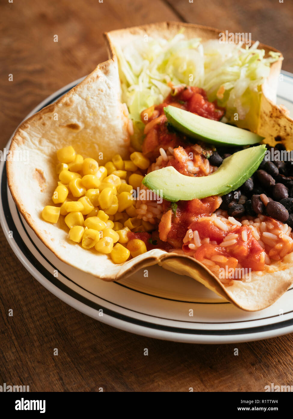 Mexikanischen taco Schüssel mit Kopfsalat, Mais, Mexikanische würzig, Tomate, Reis, schwarze Bohnen, Salsa und Avocado auf einem Mehl Tortilla. Stockfoto